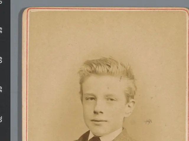 The image shows an old photo of a young man wearing a suit and tie. His face is clearly visible,...