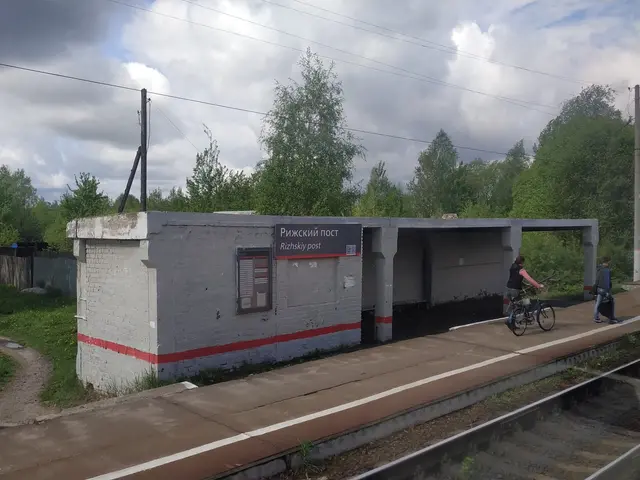 The image shows a person riding a bicycle on a train track next to a platform, with a shed in the...