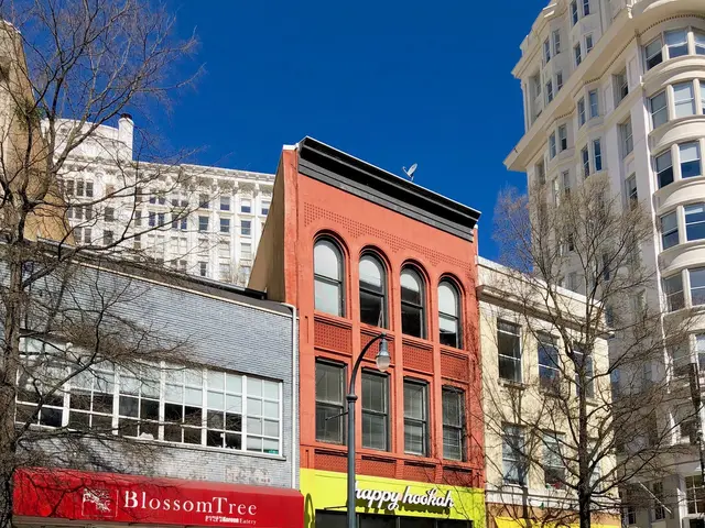 The image shows a city street with tall buildings on both sides of it, street poles, street lights,...