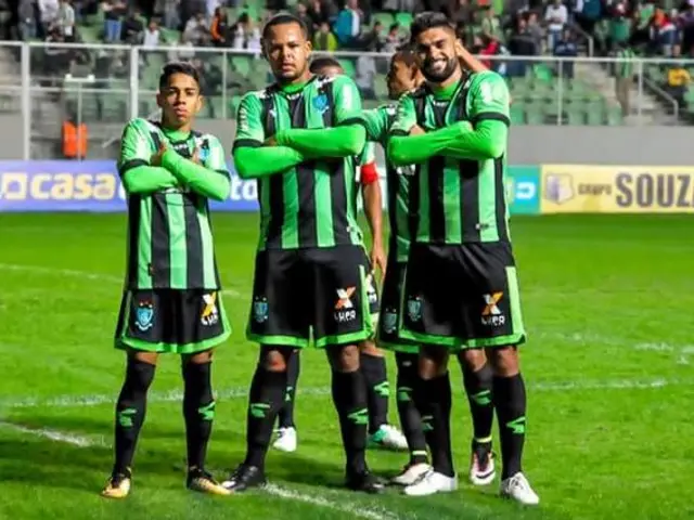The image shows a group of men standing on top of a soccer field, wearing green and black colored...