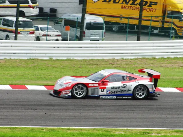 The image shows a sports car driving down a race track with a truck in the background. The track is...