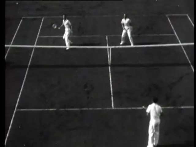 The image shows two men playing tennis on a black and white court. They are both holding rackets in...