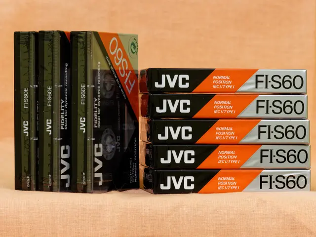 The image shows a stack of VHS tapes sitting on top of each other on an orange cloth. The tapes are...