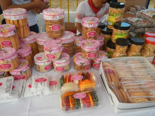 The image shows a group of people standing around a table filled with a variety of food items,...