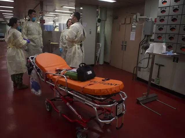 The image shows a group of people in protective gear standing around a gurney in a hospital room....