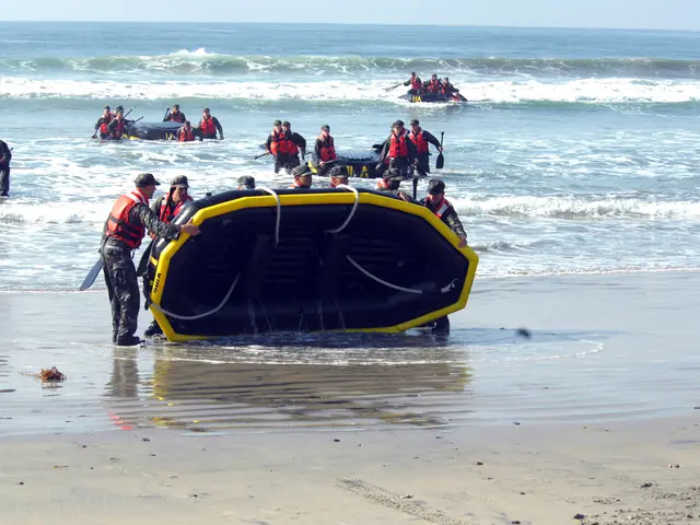 The image shows a group of people standing on top of a beach next to a boat, with the sea in the...
