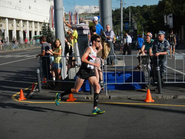 The image shows a man running in a marathon on a city street, surrounded by a group of people...