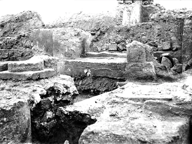 The image shows a black and white photo of the ruins of a building, with a few rocks scattered...