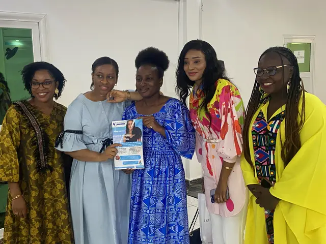 The image shows a group of women standing next to each other in a room, smiling and holding books...