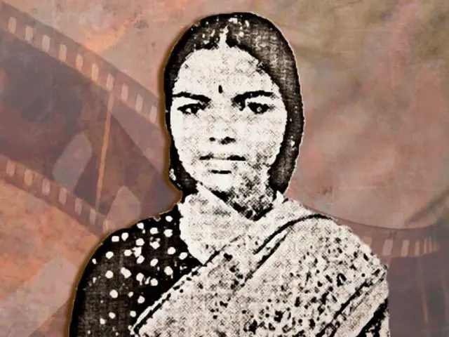 The image shows a woman in a sari standing in front of a film strip, with a blurred background. The...