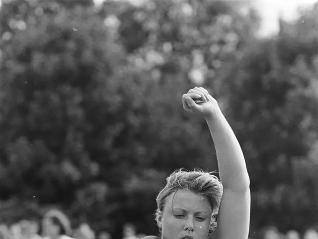 The image shows a woman throwing a discus in a track and field event, with a number on her dress....