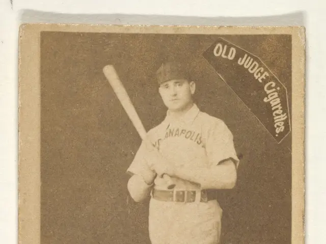 The image shows an old photo of a baseball player standing and holding a bat in his hands. He is...