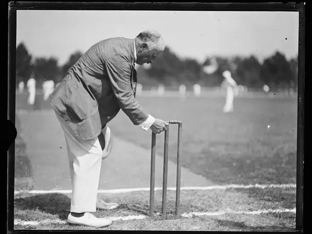 The image shows an old black and white photo of a man playing a game of cricket. He is standing on...