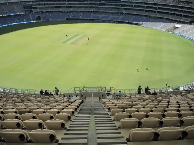 The image shows a large stadium filled with lots of people watching a game of cricket. The ground...