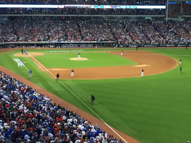 The image shows a baseball game being played in a large stadium, with a group of people standing on...