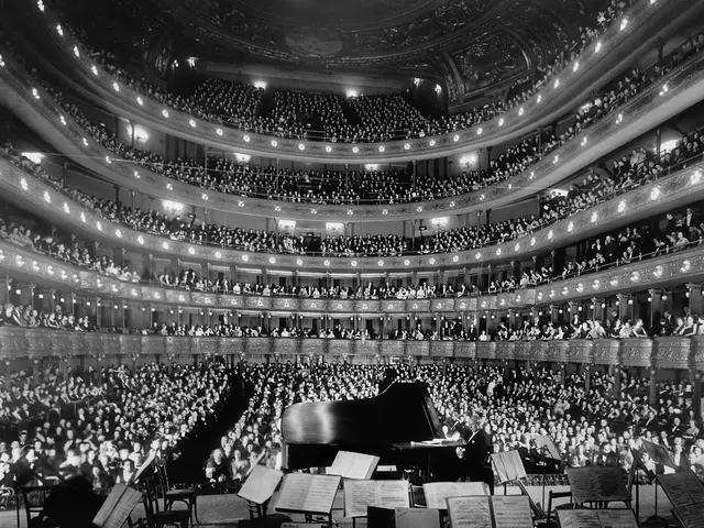 The image shows a large auditorium filled with lots of people watching a concert. There is a grand...