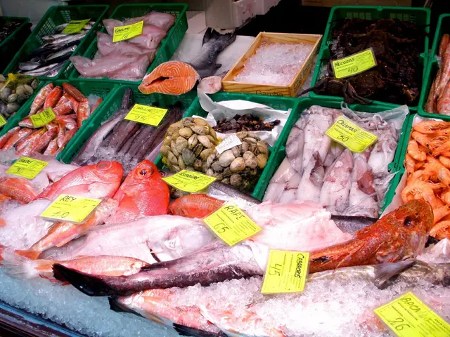 The image shows a fish market with a display case filled with lots of different types of fish on...