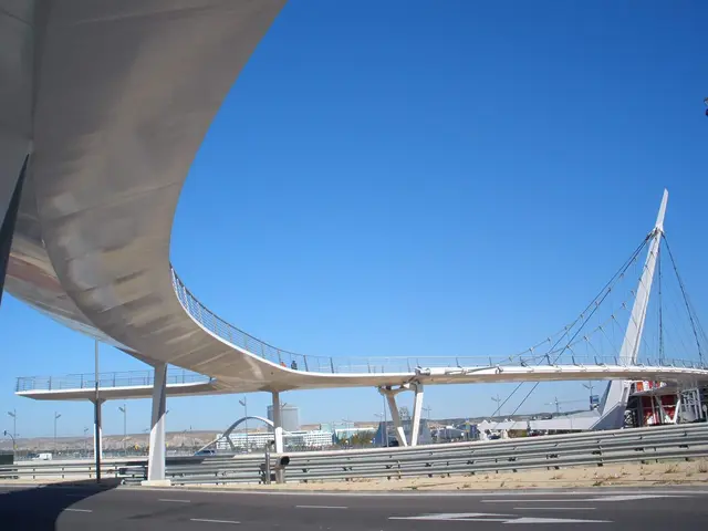 The image shows a large bridge spanning a highway with a lot of traffic on it. The bridge has...