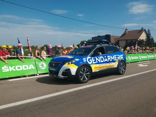 The image shows a police car driving down a road next to a crowd of people, some of whom are...