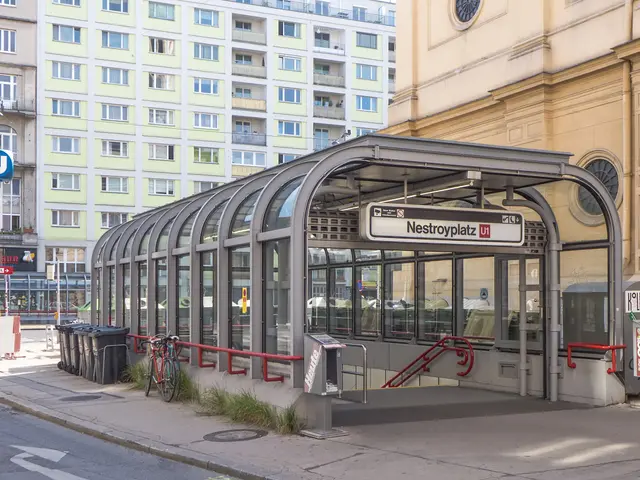 The image shows a bus stop on the side of a street next to tall buildings. There is a shed with a...