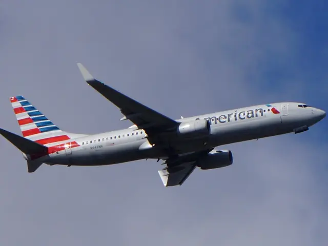 The image shows an American Airlines plane flying through a blue sky with white, fluffy clouds in...
