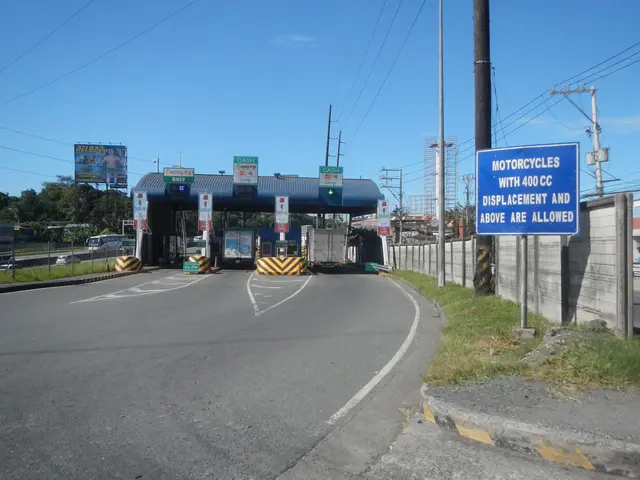The image shows a toll booth on the side of a road with a sign on it. There are vehicles driving on...