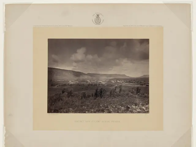 The image shows a distant view of Camp Apache in Arizona, with trees, hills, and a cloudy sky in...