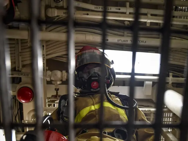 The image shows a firefighter in a cage with a fire extinguisher, wearing a helmet and a gas mask....
