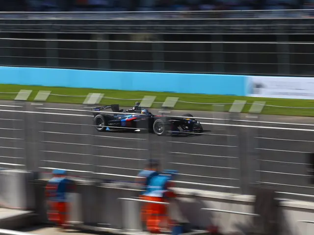 The image shows a Formula car driving down a race track with a crowd of people watching from the...