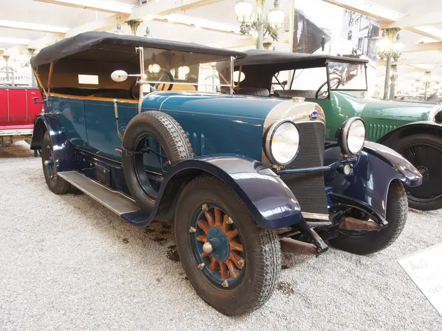 The image shows an old blue car parked in a garage next to other cars, with a board with text on...