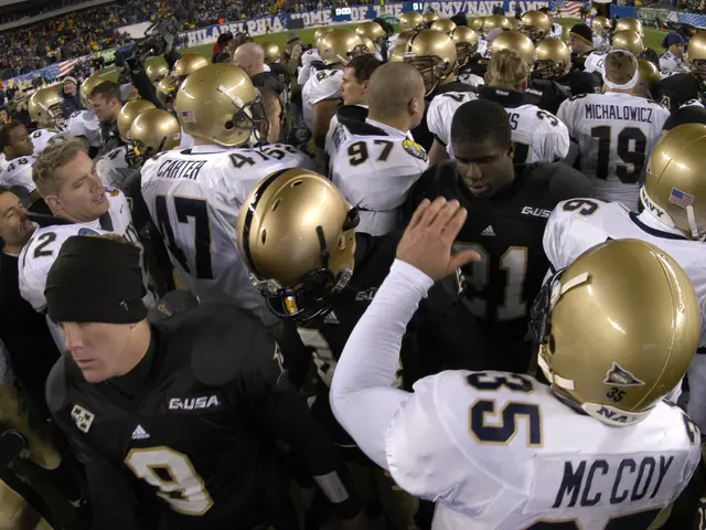 The image shows a group of football players huddled together on the field, wearing helmets and...