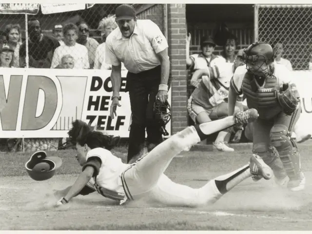 The image shows a black and white photo of a softball player sliding into home plate during a game....