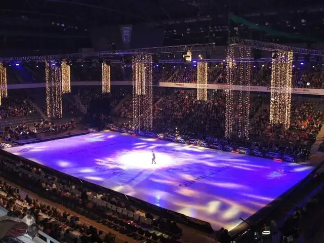 The image shows a large crowd of people sitting in a large arena, watching a figure skating event....