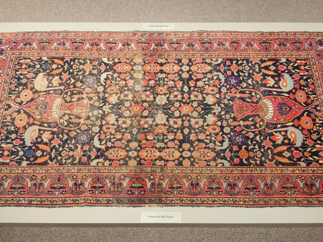 The image shows a large Persian rug on display in a museum, with a carpet on the floor. The carpet...
