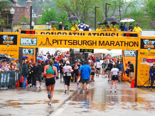 The image shows a group of people running in the Pittsburgh Marathon on a wet road surrounded by...