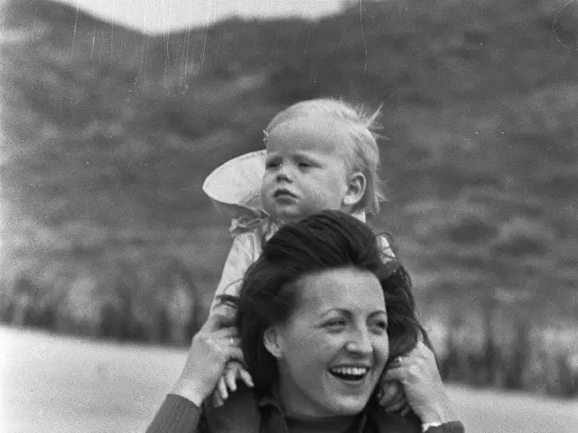 The image shows a woman with a warm smile on her face, cradling a baby in her arms. The background...