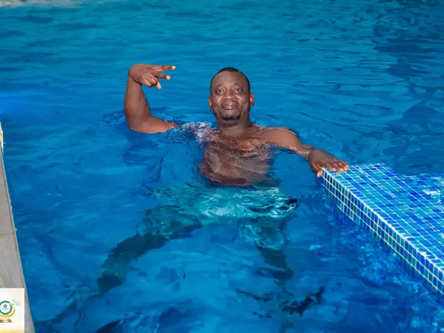 The image shows a man in a swimming pool with his arms outstretched, surrounded by a wall on the...
