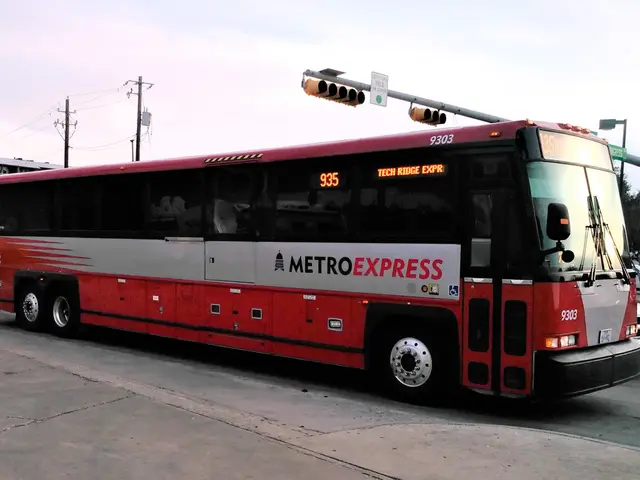 The image shows a red and white bus driving down a street next to a traffic light. There are other...