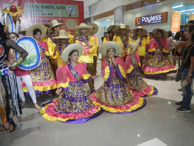 The image shows a group of people in colorful dresses and hats dancing in a mall. There are a few...