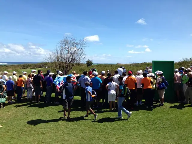 The image shows a group of people standing on top of a lush green field, some wearing caps and some...