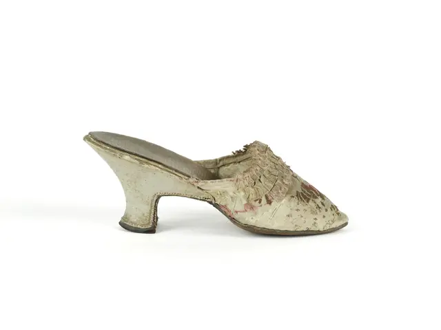 The image shows a pair of white mules on a white background. The shoes have a pointed toe and a low...