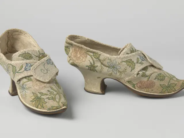 The image shows a pair of women's shoes with floral embroidery on them, resting on a white surface....