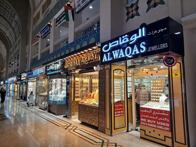 The image shows a bustling shopping mall in Dubai, UAE, with people walking on the floor, stores,...