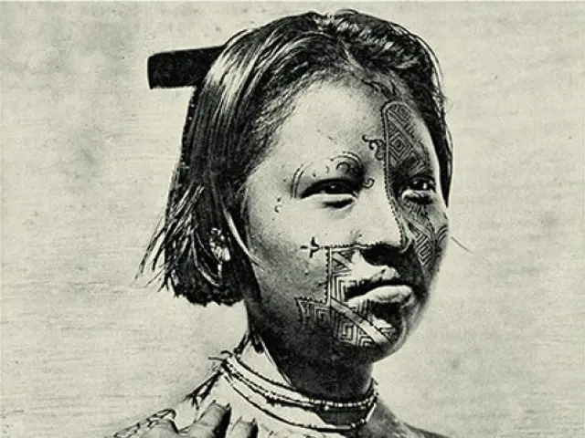 The image shows an old black and white photo of a woman with tattoos on her face and body. The...