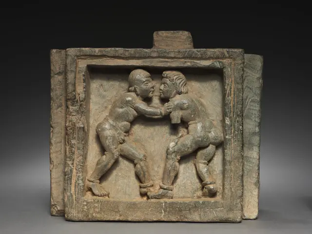 The image shows a terracotta plaque depicting two men engaged in a wrestling match. The plaque is...