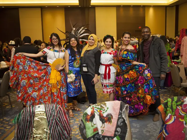 The image shows a group of people standing next to each other in colorful dresses, smiling and...