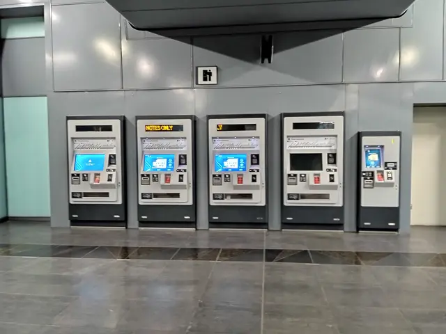 The image shows a row of automated teller machines in an airport terminal. The machines are...