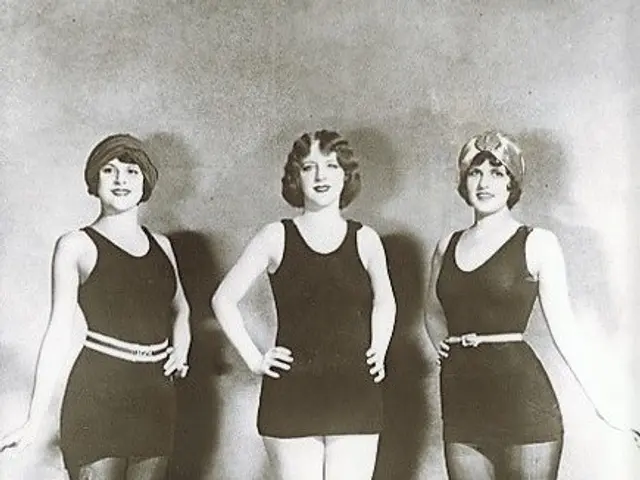 The image shows three women in bathing suits standing next to each other on the floor in front of a...