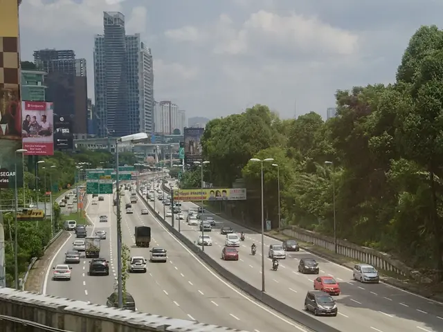 The image shows a highway filled with lots of traffic next to tall buildings, street poles, street...