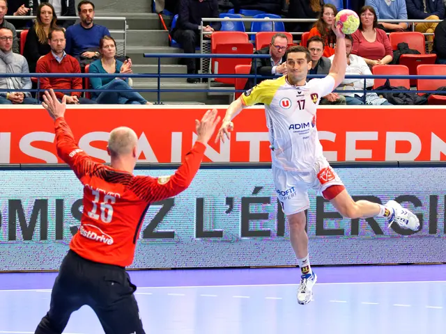 The image shows two men playing a game of handball on a court, with a ball in the air. In the...